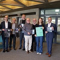 Eine Gruppe von Personen steht zusammen, alle halten Plakate oder Broschüren in den Händen.