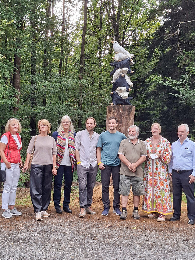 Acht Personen stehen vor einer Skulptur im Wald.