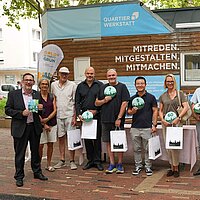 Viele Personen mit Auszeichnungen in Form von Hausnummern stehen vor einem Tiny House.