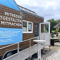 Ein holzverkleidetes Tiny House steht auf einem Platz.