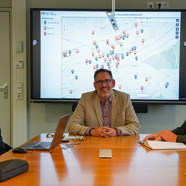 Baubürgermeister Tobias Volle (Mitte), Uwe Weiss, Leiter der Abteilung Straßenneubau und Verkehrstechnik im Grünflächen- und Tiefbauamt (rechts) und Johannes Halvaci, Leiter der Koordinierungsstelle, stellten die neue Baustellenübersicht der Stadt Pforzheim vor.  Sie sitzen vor einem großen Bildschirm auf dem die Baustellen auf einer Karte gezeigt werden. - Copyright: Stadt Pforzheim