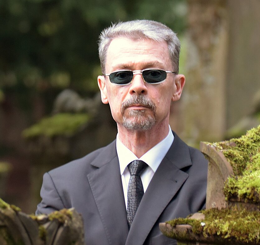 Fotografie von einem Mann mit grauen kurzen Haaren und Bart. Er trägt eine Sonnenbrille und einen Anzug. - copyright: Alessio Guerrini - Ersteller: Alessio Guerrini