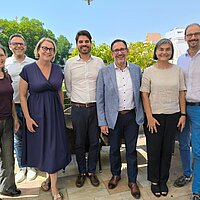 Sieben Personen auf einem Gruppenfoto, im Hintergrund ist ein blauer Himmel zu erkennen.