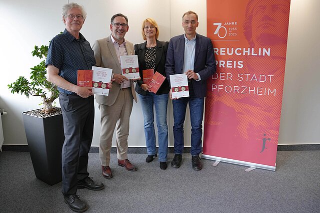Vier Personen stehen vor einem orangenen Banner und halten Bücher in den Händen.