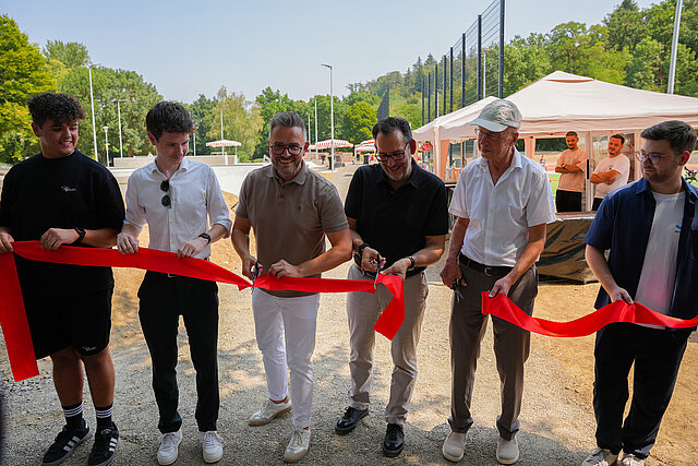 Oberbürgermeister Peter Boch (Dritter von links), Bürgermeister Frank Fillbrunn (Zweiter von rechts) sowie Bürgermeister Tobias Volle (Dritter von rechts) und der Vorsitzende des Jugendgemeinderats, Leon Meyer (Zweiter von links), schneiden ein rotes Band durch und weihten die neue Sport- und Freizeitanlage im Enzauenpark mit weiteren Vertretern des Jugendgemeinderats ein.