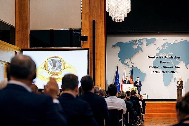 Viele Menschen sitzen in einem Saal und schauen auf die Bühne wo der Ring übergeben wird