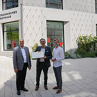 Ihab Mousa, Prokurist der Stuttgarter Niederlassung von Ten Brinke, Baubürgermeister Tobias Volle sowie Daniel Scheufler, Schlossberghöfe-Projektkoordinator der Stadt, präsentieren stolz das DGNB-Gold-Zertifikat vor der Fassade des neuen Technischen Rathauses.