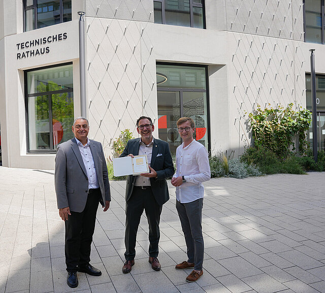 Ihab Mousa, Prokurist der Stuttgarter Niederlassung von Ten Brinke, Baubürgermeister Tobias Volle sowie Daniel Scheufler, Schlossberghöfe-Projektkoordinator der Stadt, präsentieren stolz das DGNB-Gold-Zertifikat vor der Fassade des neuen Technischen Rathauses.