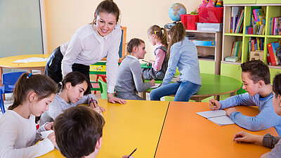 Lehrerin/Betreuerin in einem Raum mit Grundschülern.
