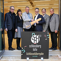 Gruppenbild Verantwortliche des Projektes Schlossberghöfe vor Logo mit symbolischem Schlüssel 