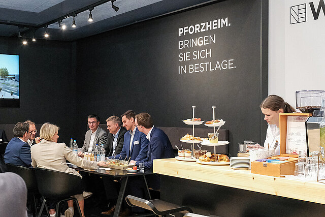 Farbfoto: Menschengruppe sitzt am Tisch auf dem Pforzheimer Messestand