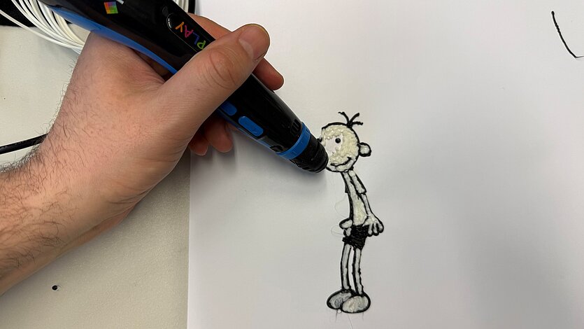 Eine Hand hält einen 3D-Stift und zeichnet eine kleine schwarz-weiße Comicfigur auf ein weißes Blatt Papier. - copyright: Stadtbibliothek Pforzheim - Ersteller: Stadtbibliothek Pforzheim
