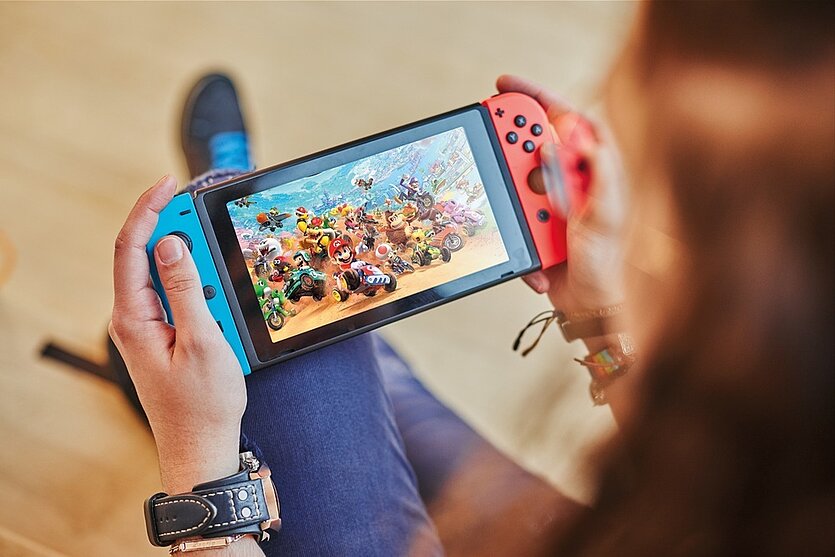 Fotografie: die Konsole Nintendo Switch wird in zwei Händen gehalten. Es wird darauf ein Rennspiel gespielt. - copyright: Stadtbibliothek Pforzheim - Ersteller: Daniel Foltin