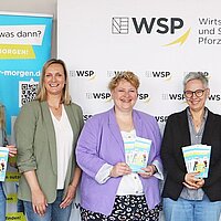 Viele Personen, die Flyer in den Händen halten, stehen vor Werbebannern.