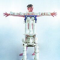 Eine Person steht hinter einer aus Porzellan Gefäßen nachgebauten Person.