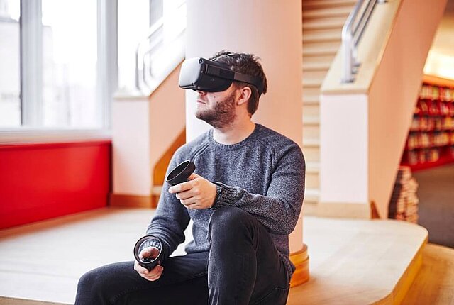 Fotografie von einer sitzenden Person mit einem VR-Set tragend - copyright:Stadtbibliothek Pforzheim