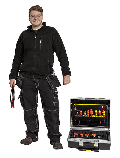 Symbolbild: Azubi für Elektroniker für Betriebstechnik in Arbeitskleidung und mit Werkzeugkoffer