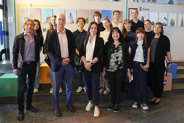 Eine Gruppe von Personen steht vor einer Wand, an der Bilder hängen.