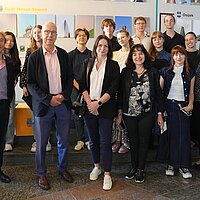 Eine Gruppe von Personen steht vor einer Wand, an der Bilder hängen.