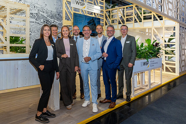 Eine Gruppe von Personen steht vor einem Messestand.