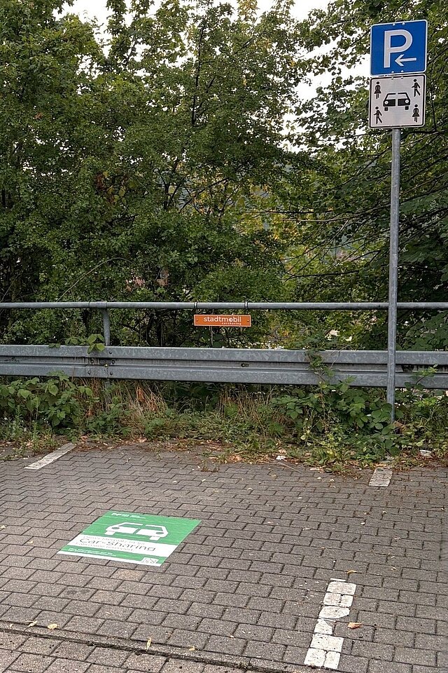 Ein Parkplatz mit einem Grünen, großen Aufkleber auf dem Boden. Im Hintergrund sind Bäume zu sehen.