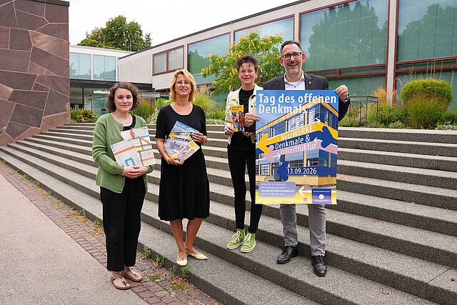 Vier Personen auf einer Treppe halten Plakate und stehen vor dem Schmuckmuseum.