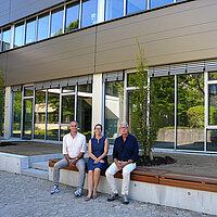Drei Personen sitzen auf einer Bank vor der neuen Fassade der Heinrich-Wieland-Schule in Pforzheim