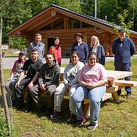 Viele Personen sitzen auf und stehen hinter einer Sitzgarnitur