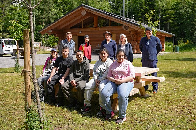 Viele Personen sitzen auf und stehen hinter einer Sitzgarnitur