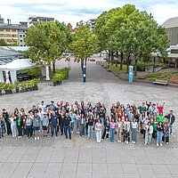 Viele Jugendliche auf einem Platz winken in die Kamera. Das Bild ist von oben aufgenommen.