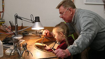 Im Technischen Museum: Mann zeigt Kind Technik am Goldschmiedetisch